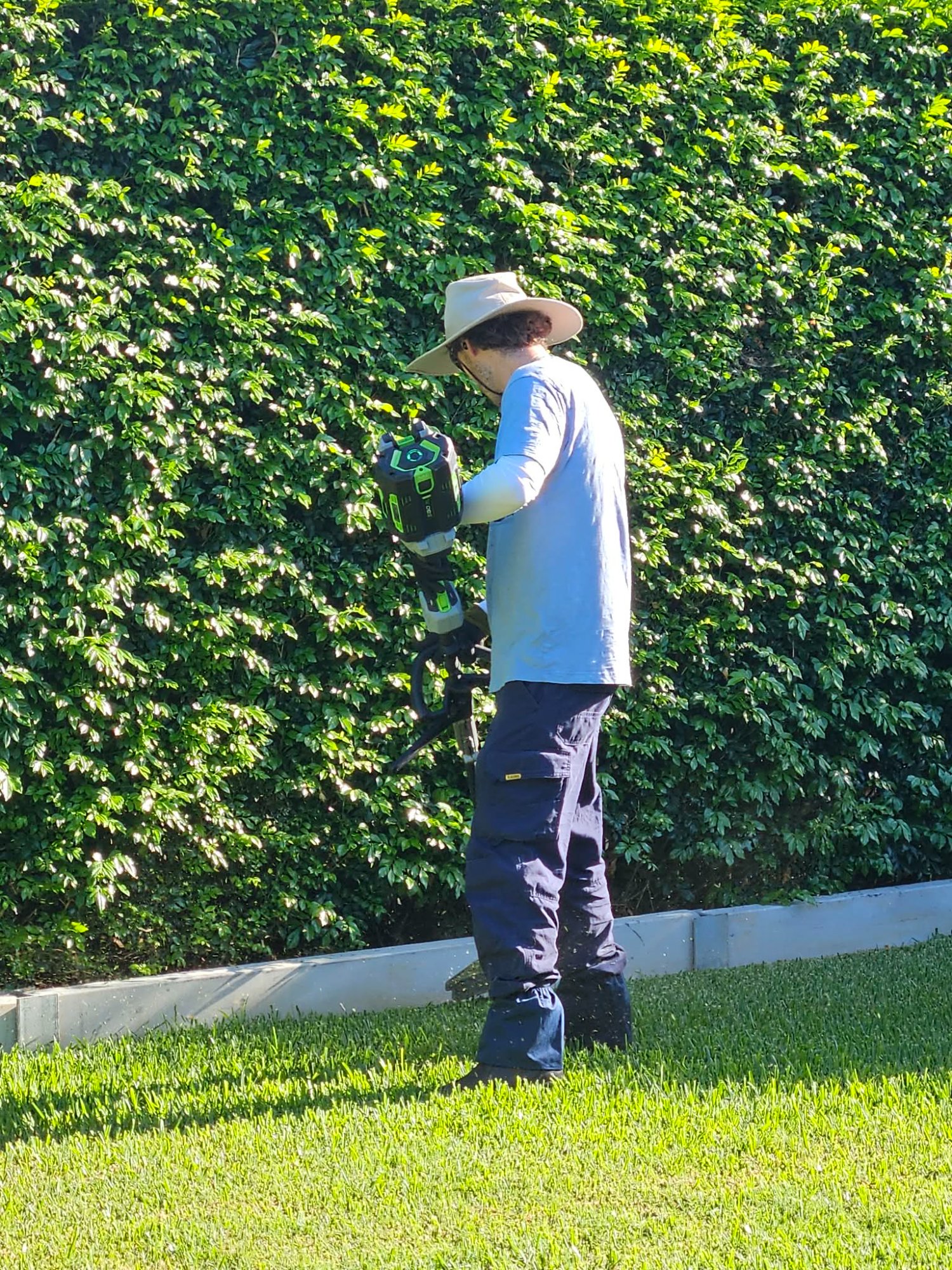 Logan, owner of BrownLeaf Electric Mowing, trimming a hedge with electric equipment